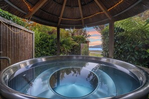 A hot tub under a thatched roof with bamboo fencing and lush greenery.