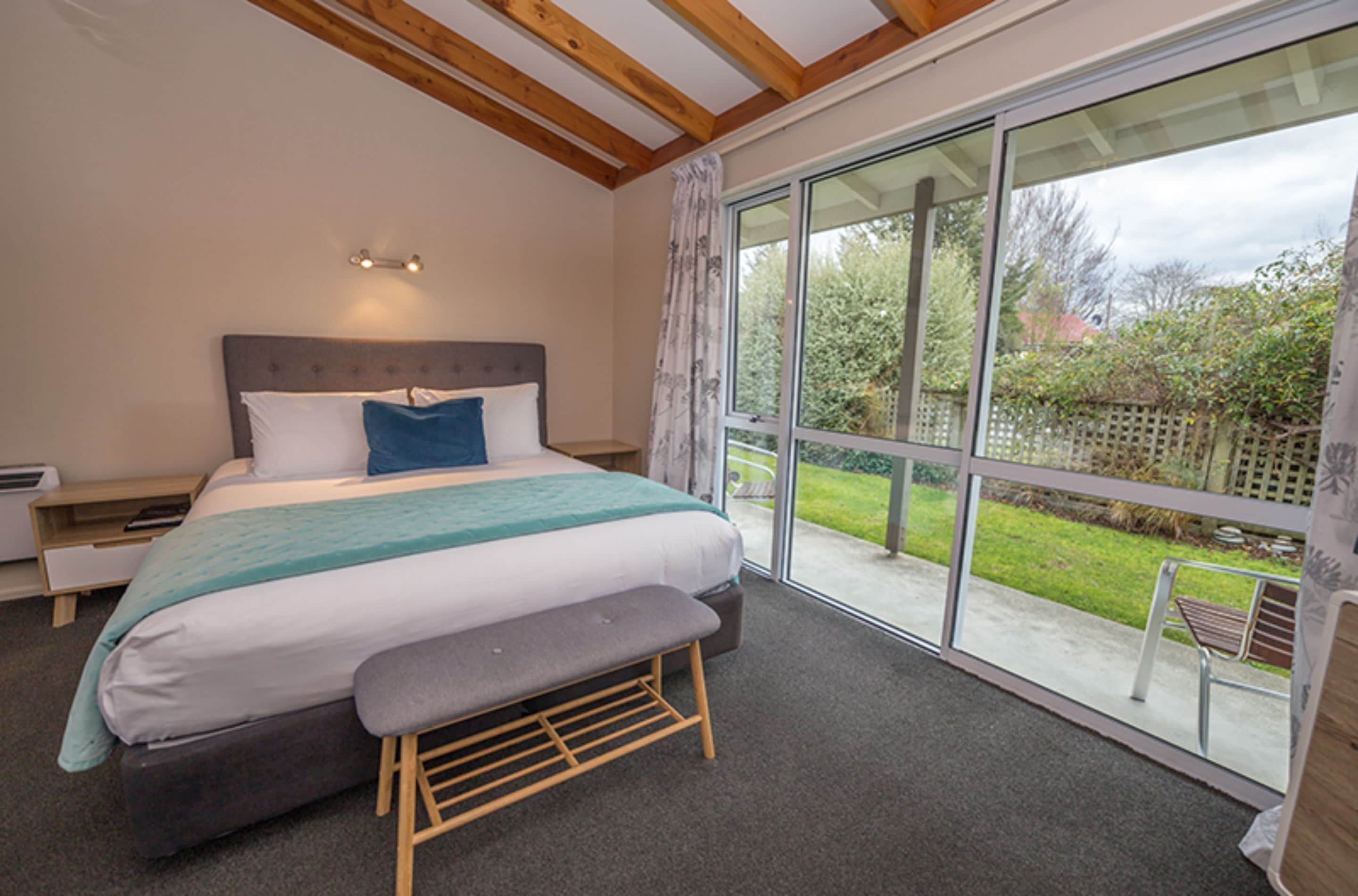 A bedroom with a large bed, a bench, a bedside table, and a window with a view of the outdoors.