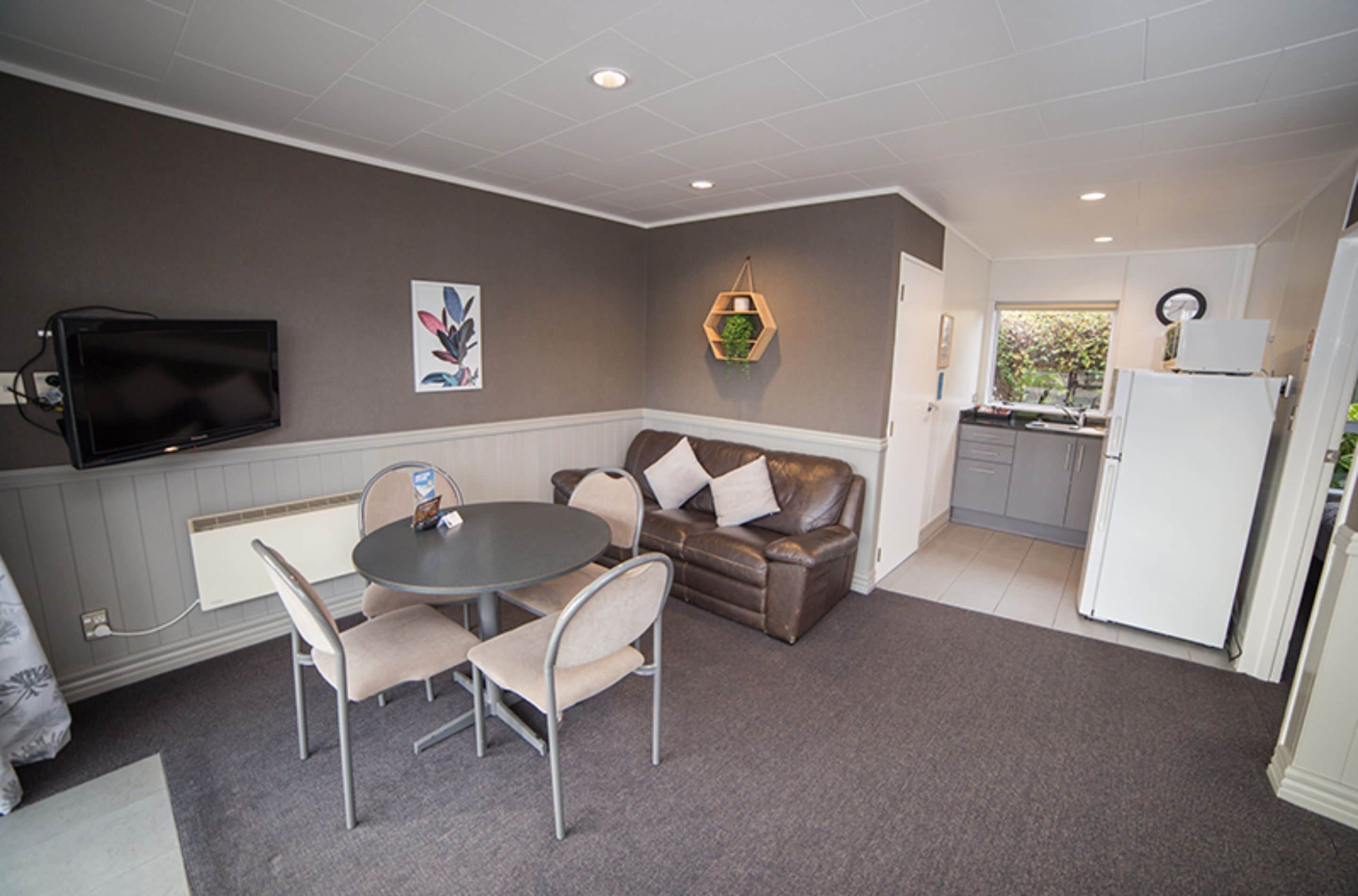 A compact living space with a dining area, a sofa, a television, and a kitchen area.