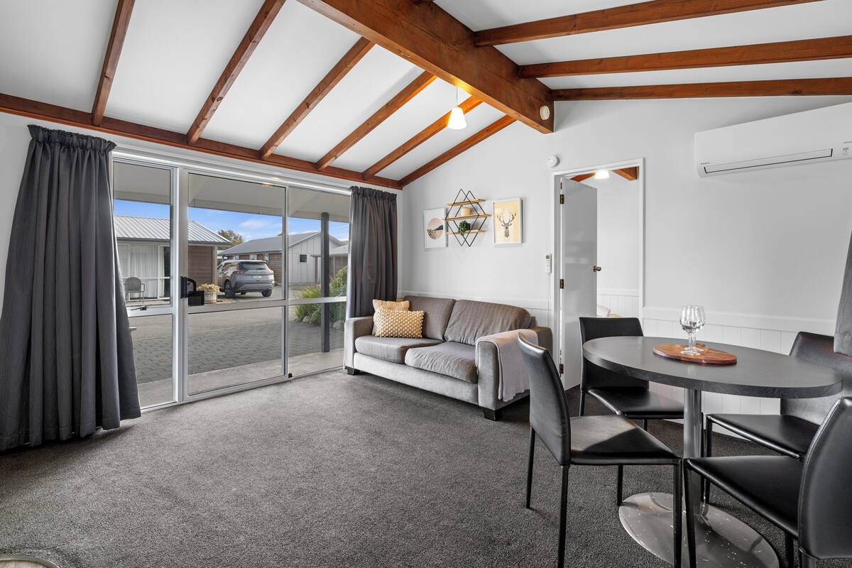 A modern living room with a sofa, a dining table with chairs, and a sliding glass door leading outside.