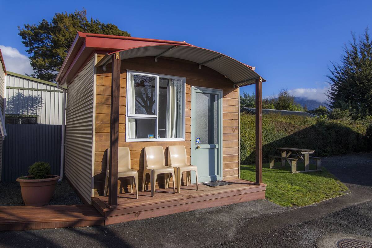A small wooden cabin with a porch, a door, and a bench outside.