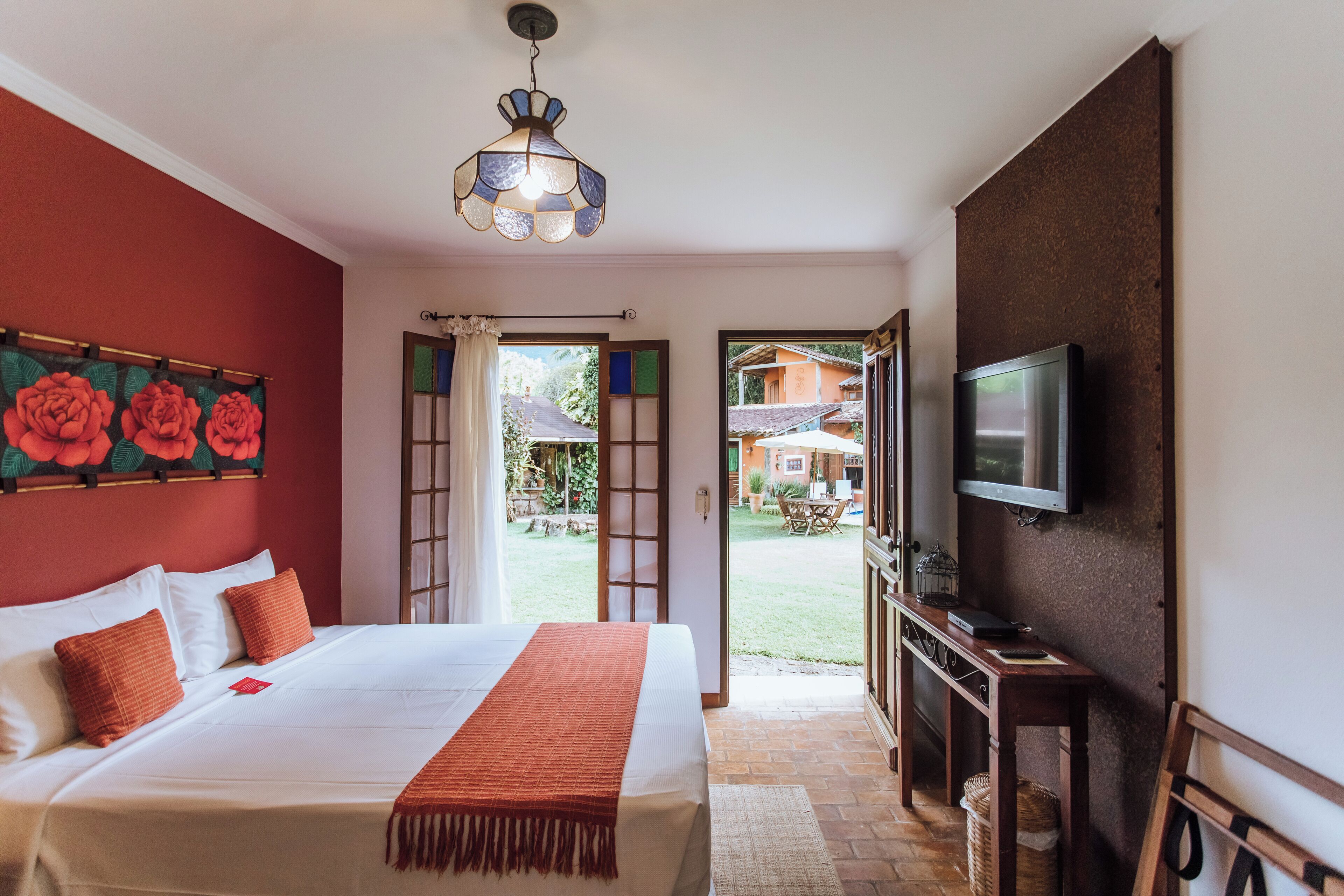 Ein Hotelzimmer mit Bett, Fernseher, roter Wand und Blick nach draußen.