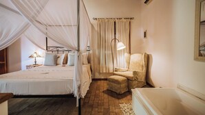 Un dormitorio con cama, una silla, una mesita de noche, una lámpara y una ventana con cortinas.