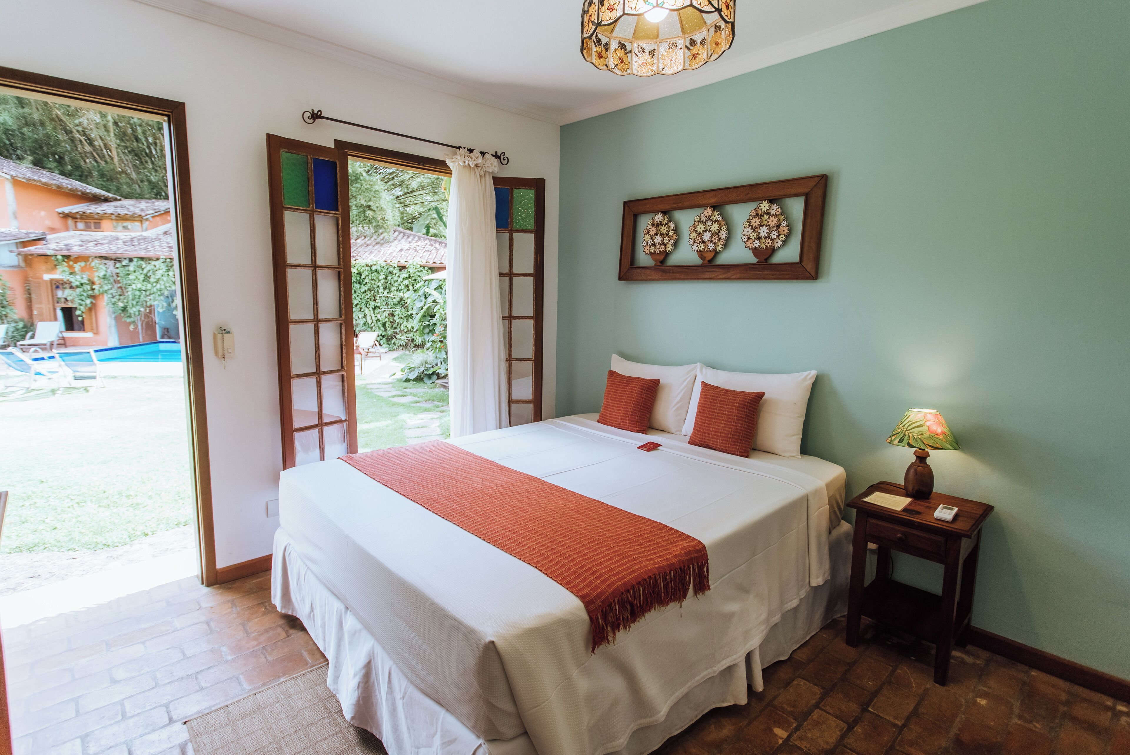 Quarto com uma cama grande, mesa de cabeceira com abajur e vista para o exterior.