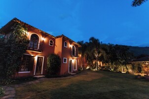 Una casa de dos pisos con fachada roja, un balcón e ingreso delantero bien iluminado.