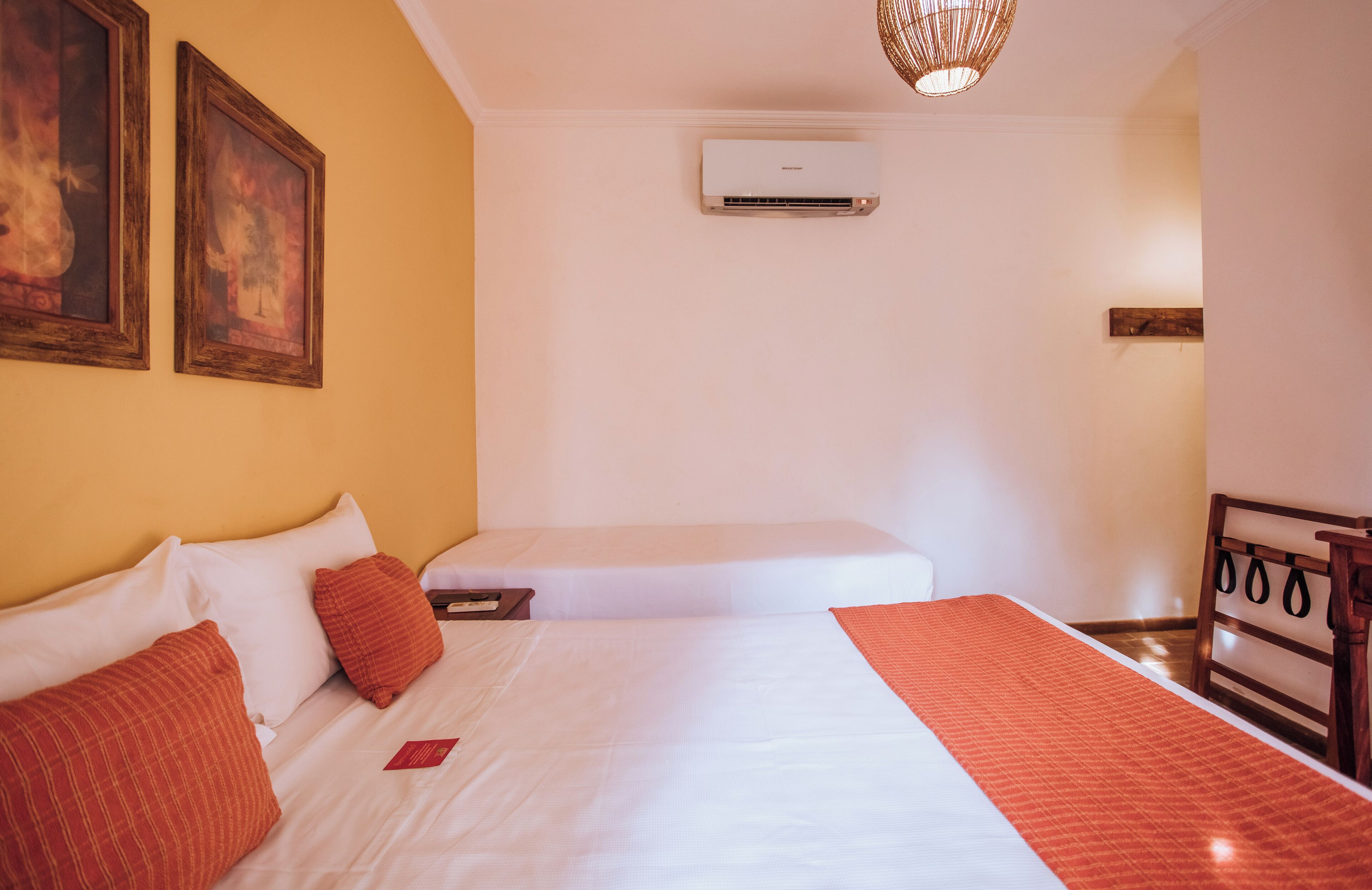 Quarto de hotel com uma cama grande, mesa de cabeceira, ar condicionado e prateleira na parede.
