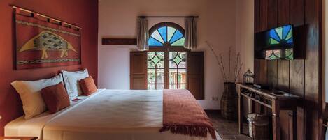 Un dormitorio con una cama grande, vigas de madera en el techo, una ventana con vistas, un televisor y un tapiz decorativo.