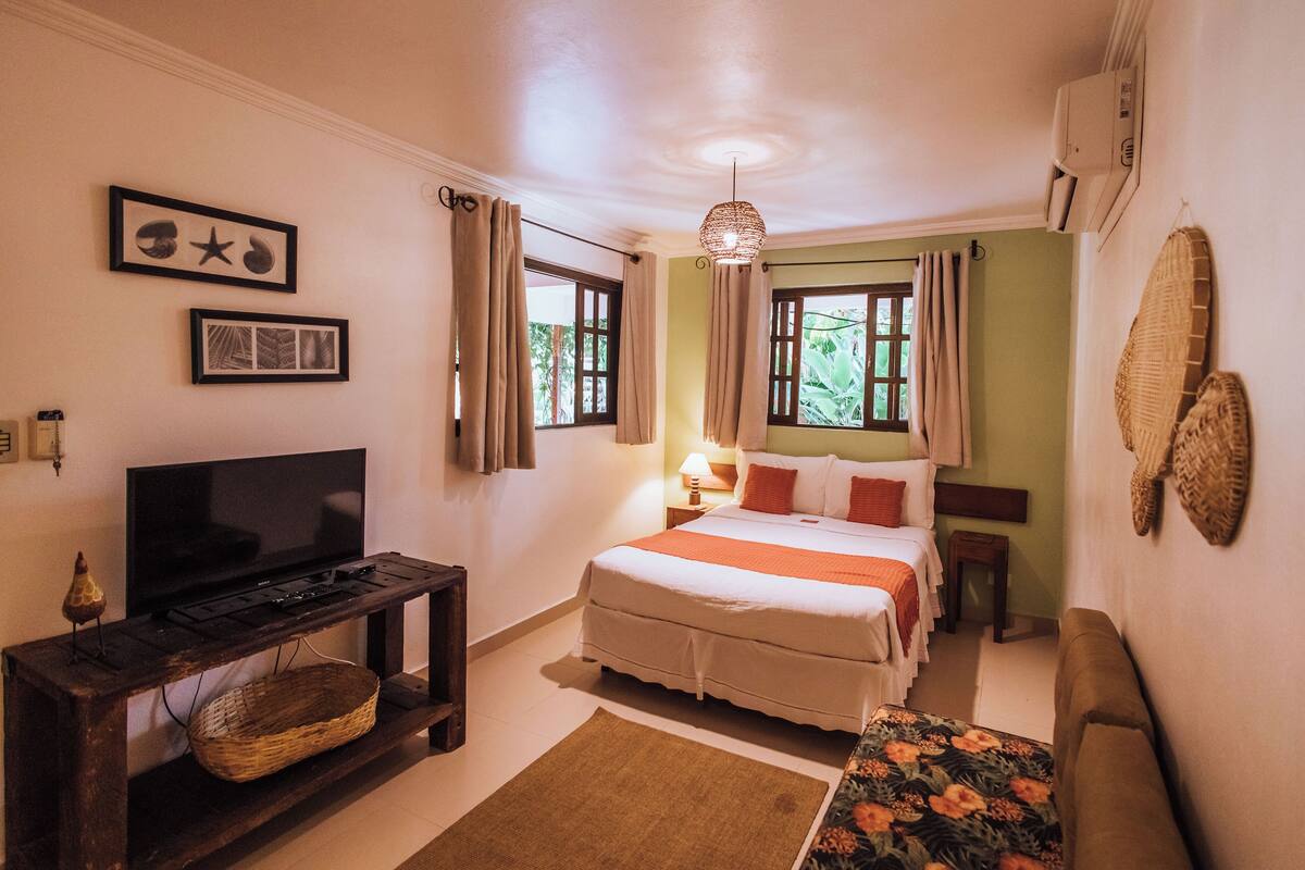 A bedroom with a bed, a TV, a lamp, and a window with curtains.