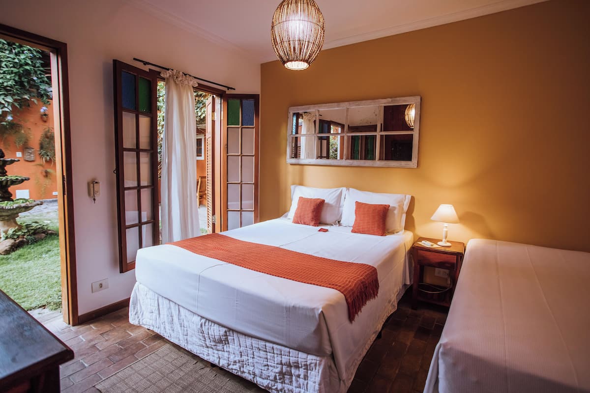 A bedroom with a large bed, a bedside table with a lamp, and a view of the garden through an open door.