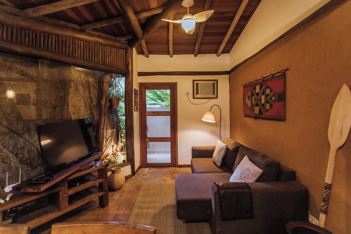 A cozy living room with a television on a wooden stand, a sofa, a ceiling fan, and a wooden spoon on the wall.
