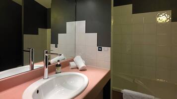 A modern bathroom with a white sink, chrome faucet, and a large mirror. There are white towels on the counter and a white towel hanging on the wall.