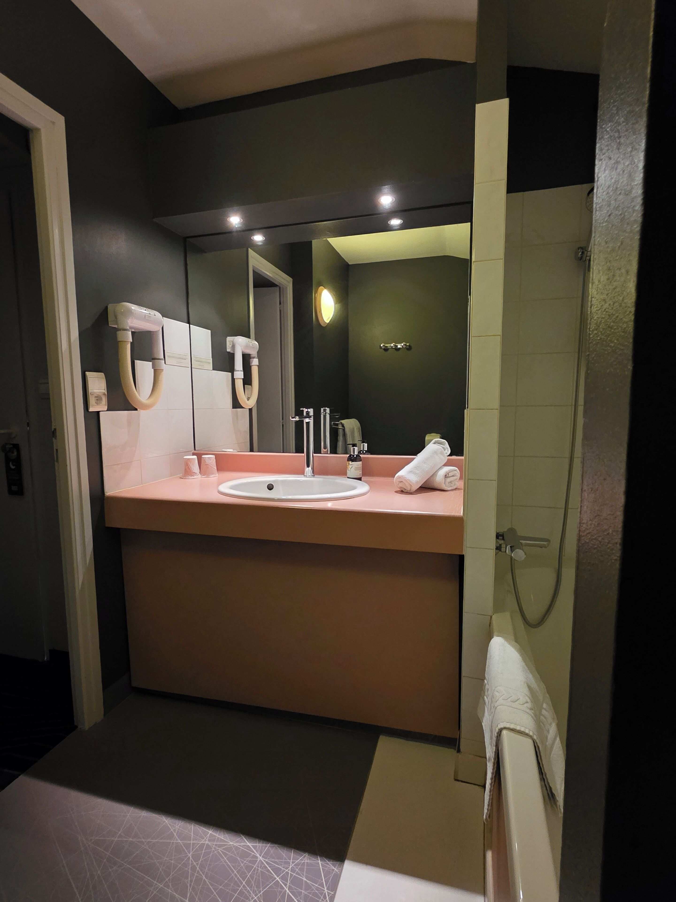A modern bathroom with a large mirror, a sink, a shower, and a towel rack.