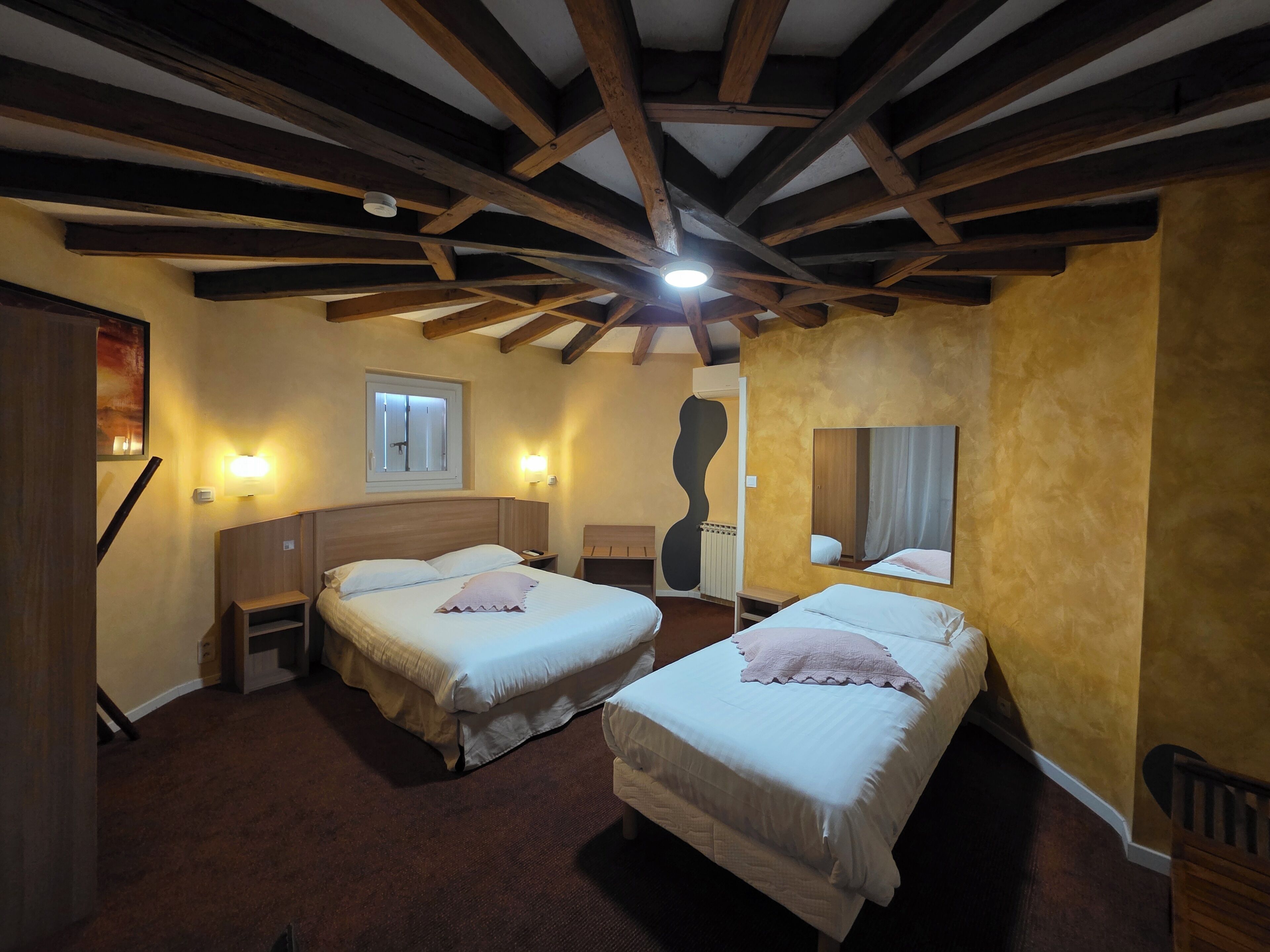 Quarto de hotel com duas camas, vigas de madeira no teto, uma janela e um radiador.
