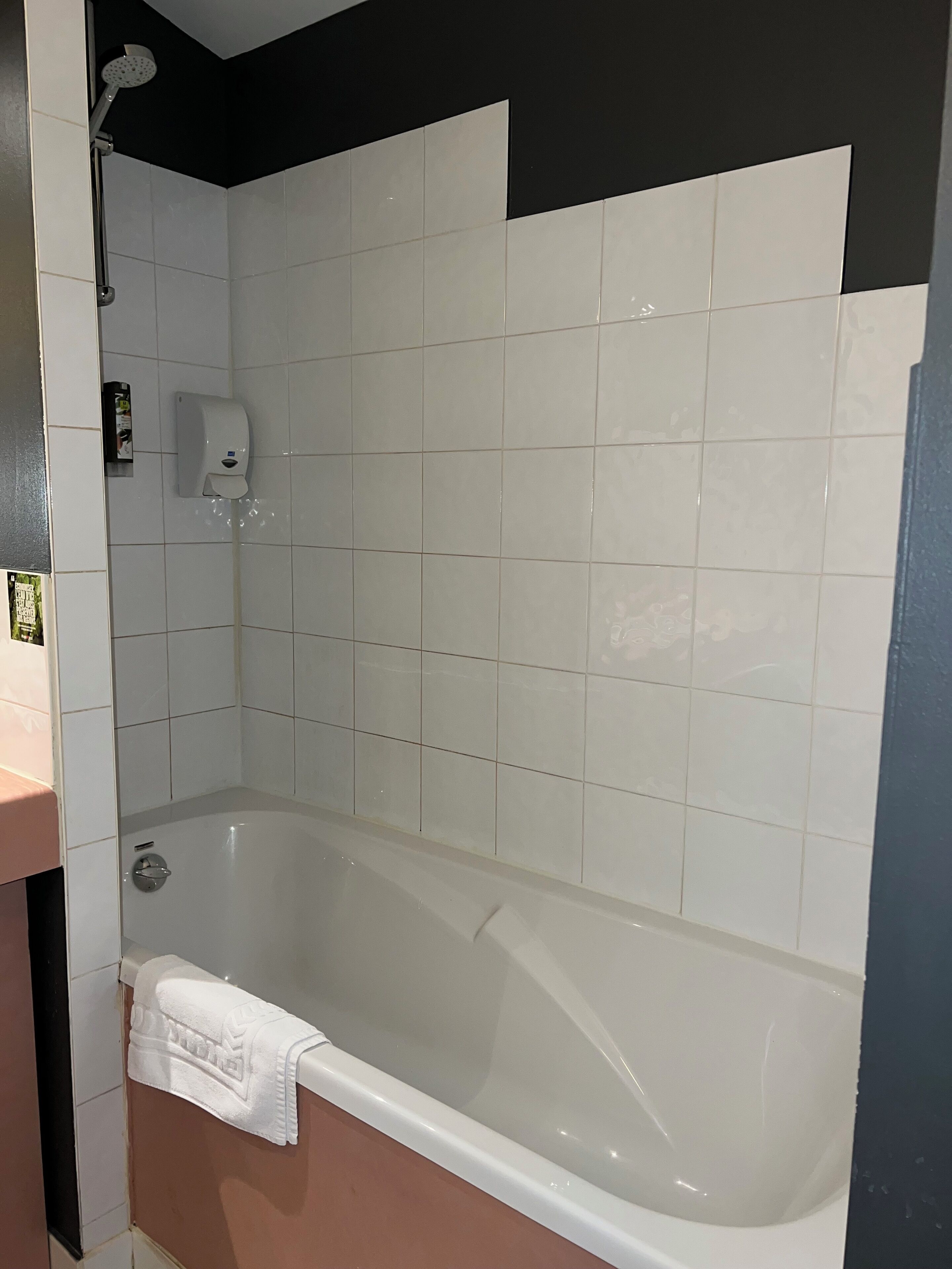 A bathroom with a bathtub, a hand soap dispenser, and a showerhead.