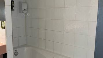A bathroom with a bathtub, a hand soap dispenser, and a showerhead.