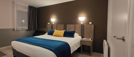 A modern hotel room with a large bed, bedside lamps, a nightstand, and a radiator.
