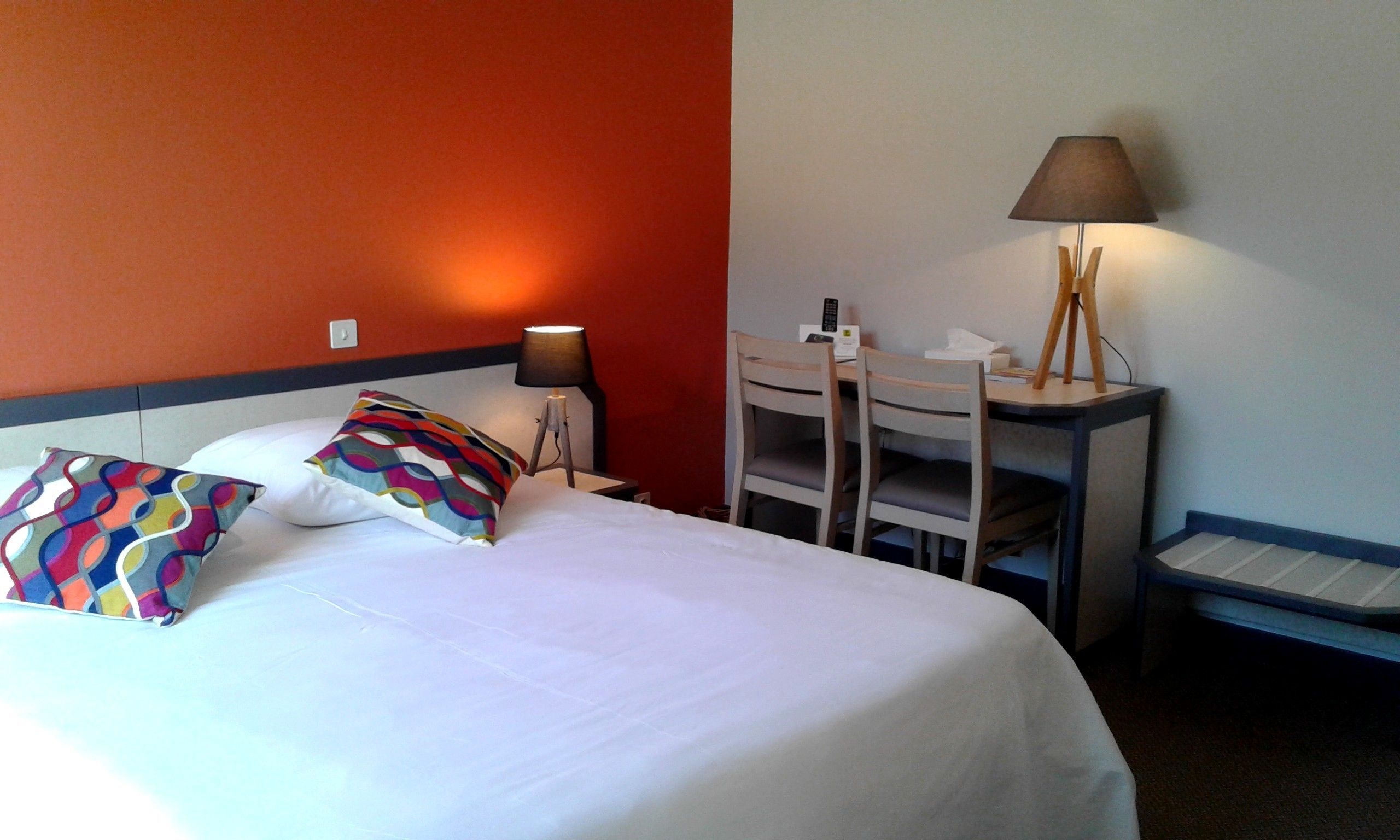 Una habitación de hotel con una cama, un escritorio, una silla y una lámpara.