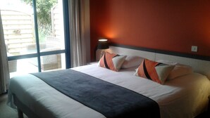 Una habitación de hotel con una cama grande, una ventana con cortinas y una mesita de noche con lámpara.