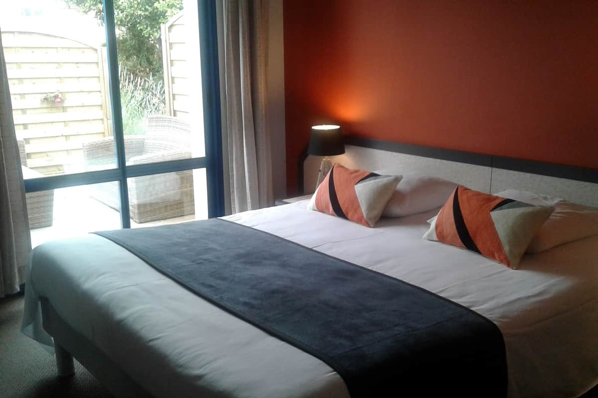 A hotel room with a large bed, a window with curtains, and a nightstand with a lamp.