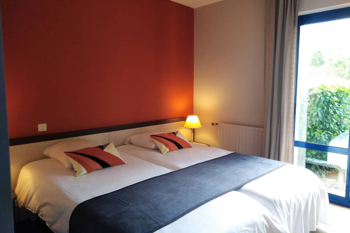 A hotel room with a bed, a nightstand with a lamp, and a window with curtains.