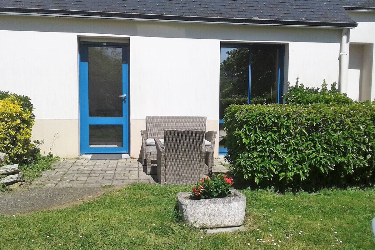 A house with a blue door, a small patio with a wicker chair, and a garden with a flower bed.