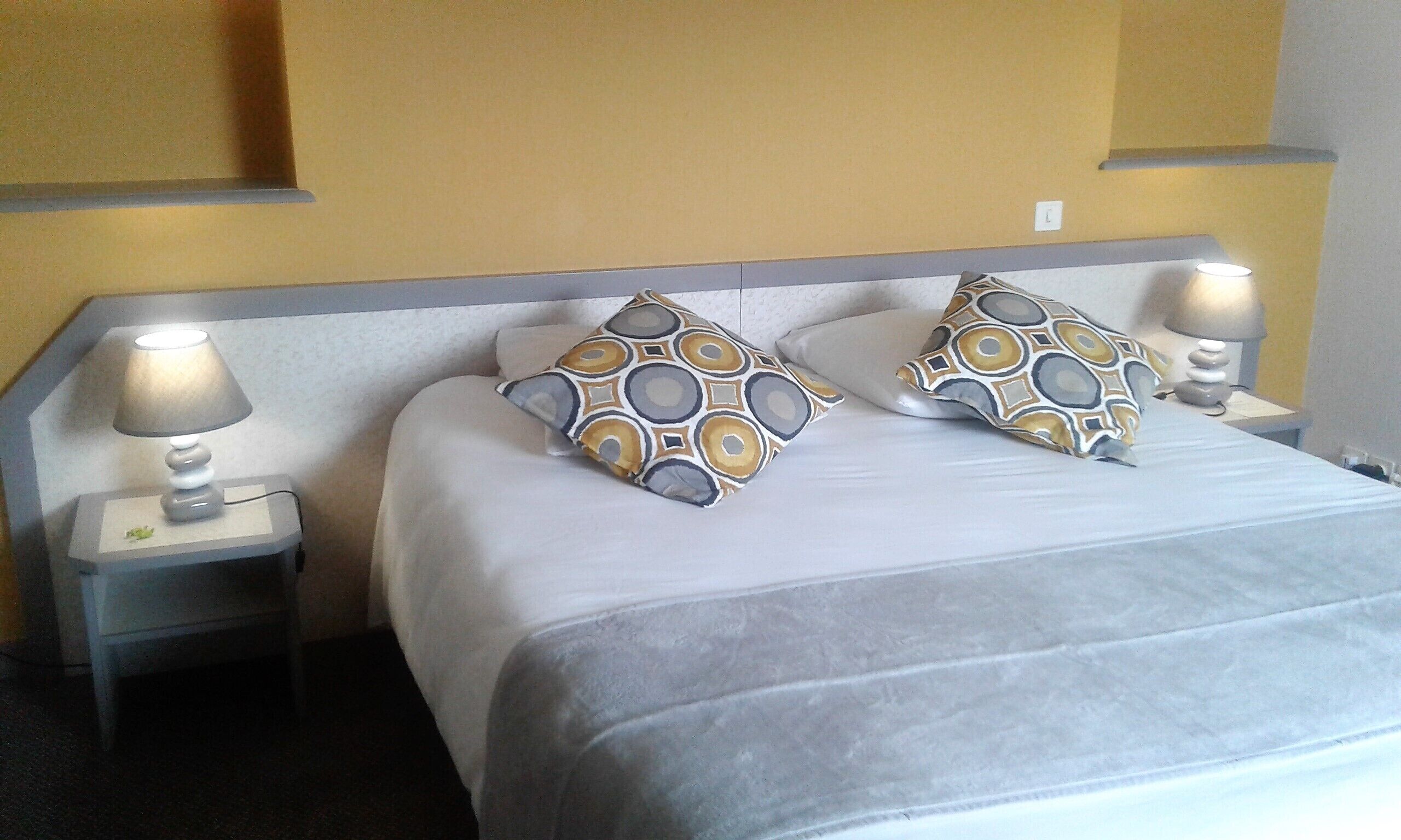 Een hotelkamer met een bed, twee gestreepte kussens, twee bedlampen en een nachtkastje met een kleine plant.