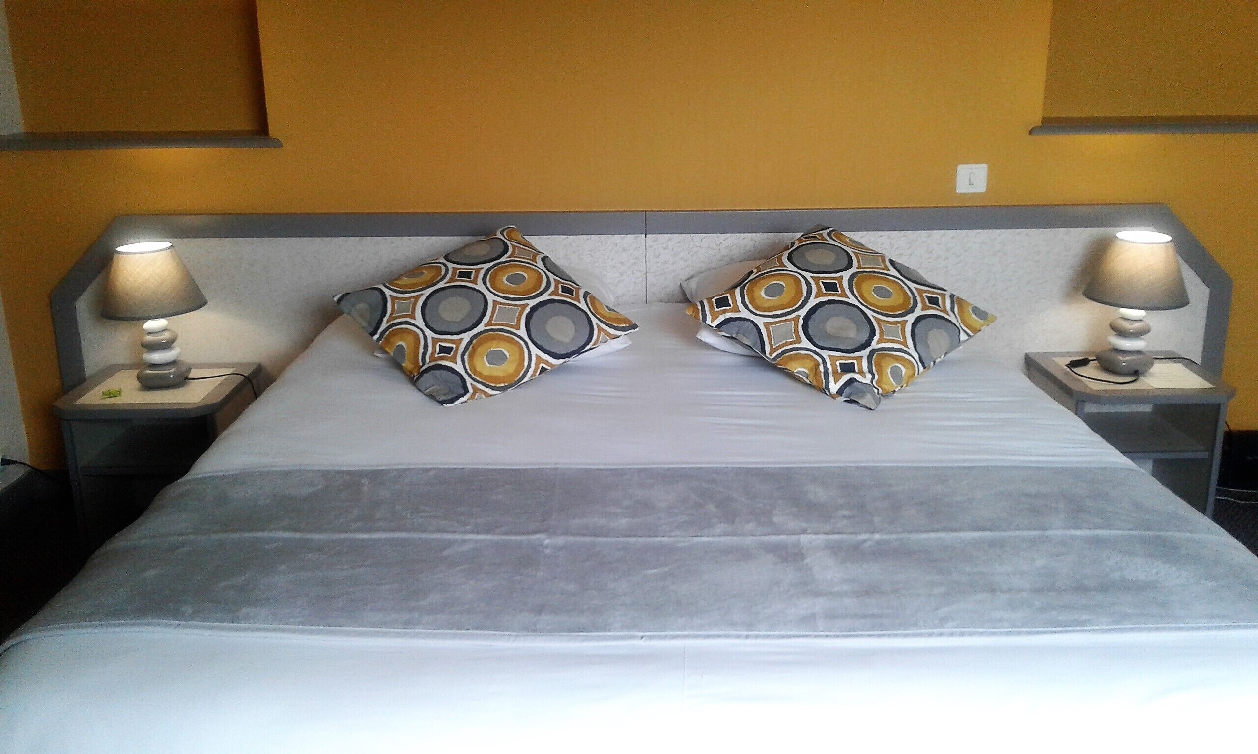 Una cama con dos almohadas estampadas, dos lámparas de noche y un cabecero de color neutro.