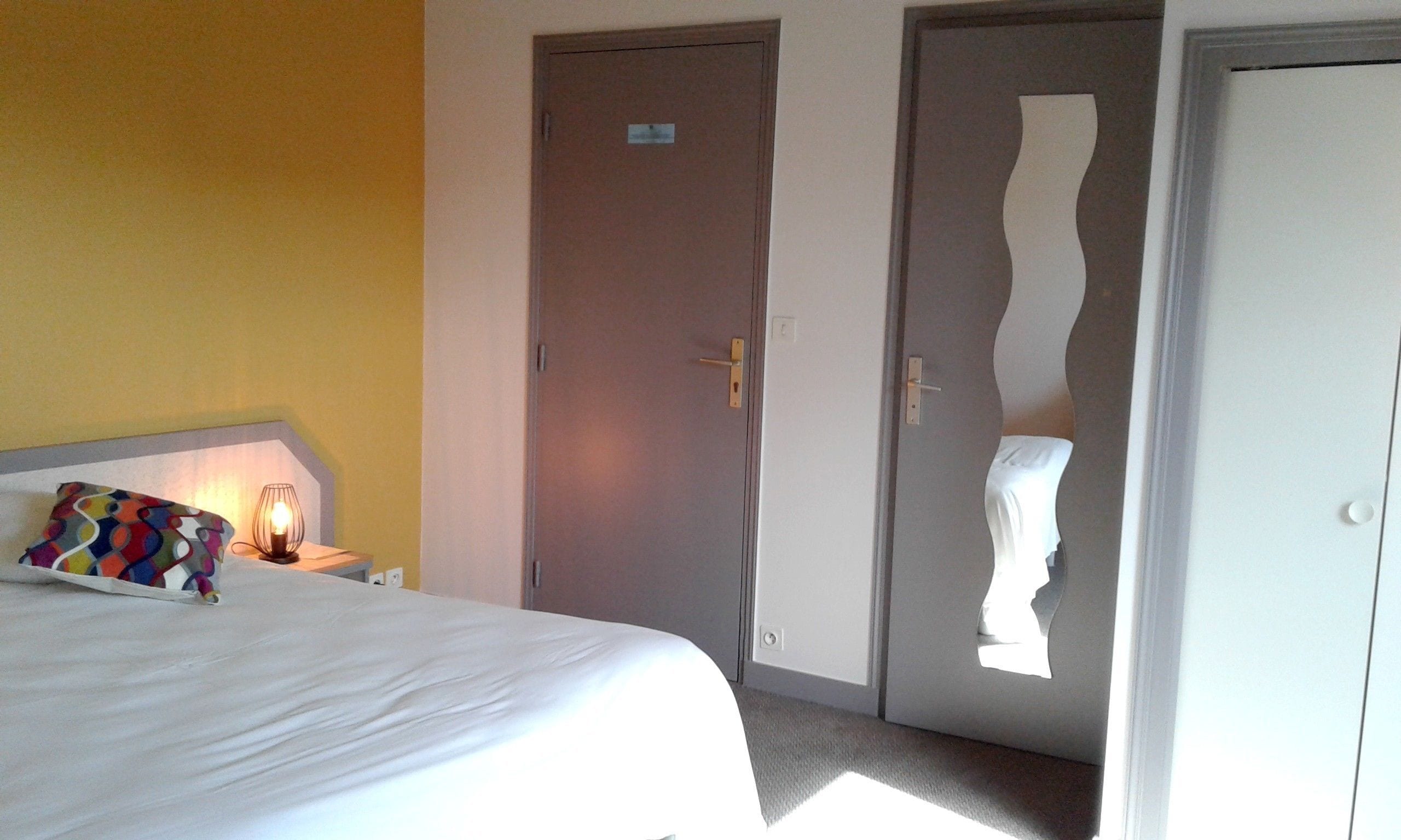 Een hotelkamer met een bed, nachtkastje, lamp en twee deuren.