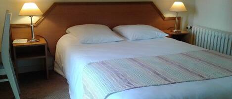 A neatly made bed with white linens and a patterned throw, flanked by two bedside lamps on wooden nightstands.
