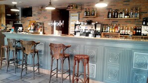 Una zona de bar con mostrador, taburetes y estantes llenos de botellas.