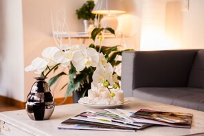 A white vase with white flowers on a table, a plate with a white cake, and magazines. - Hôtel Le Petit Manoir Provence (Les Angles)