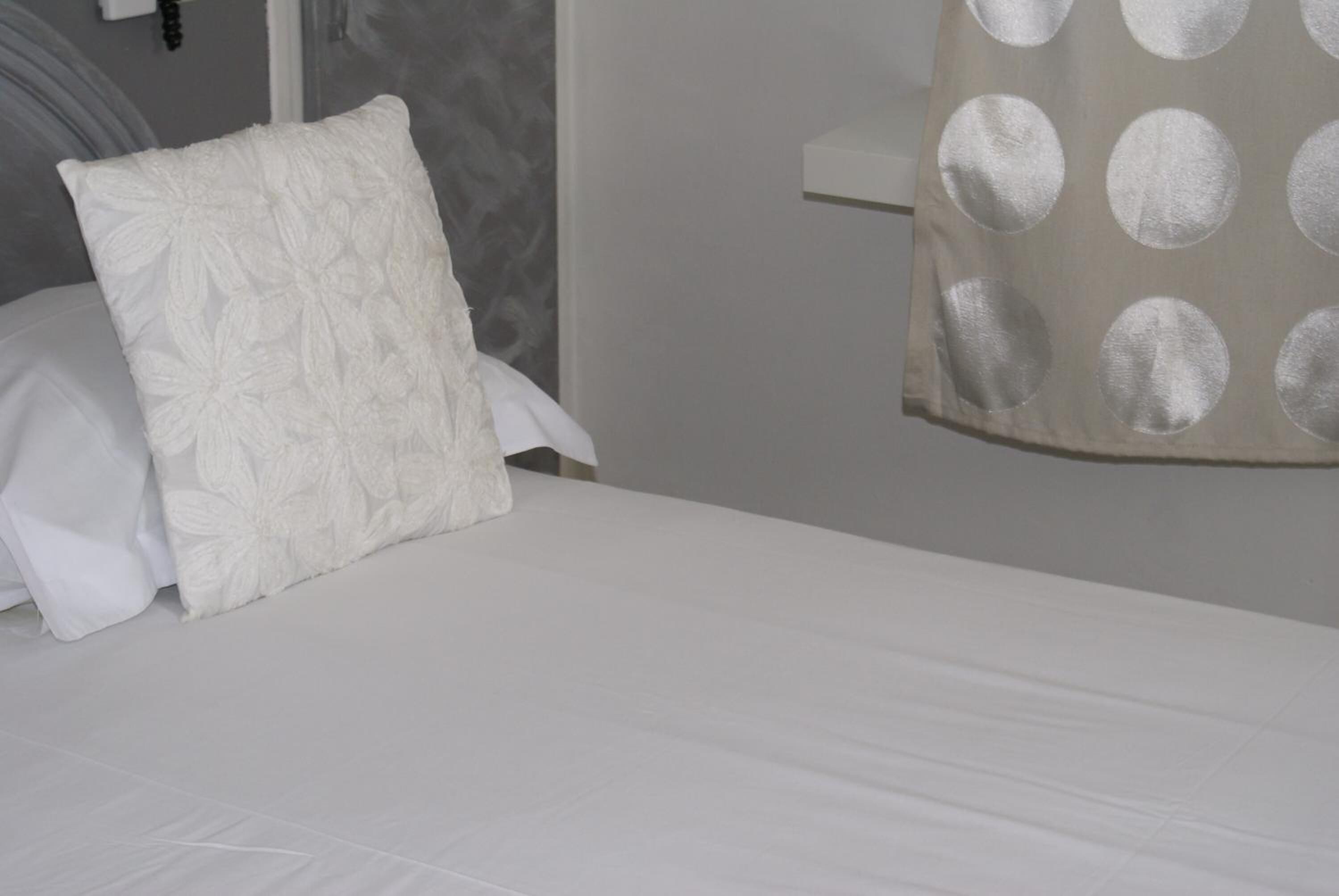 Una cama con un almohadón y una colcha blancos.