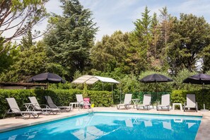 A swimming pool with lounge chairs and umbrellas, surrounded by greenery. - Hôtel Le Petit Manoir Provence (Les Angles)