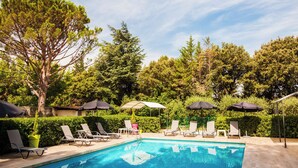 A swimming pool with lounge chairs and umbrellas, surrounded by trees and greenery. - Hôtel Le Petit Manoir Provence (Les Angles)