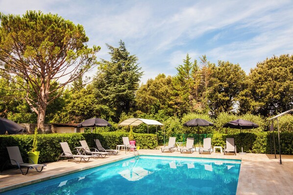 A swimming pool with lounge chairs and umbrellas, surrounded by trees and greenery. - Hôtel Le Petit Manoir Provence (Les Angles)