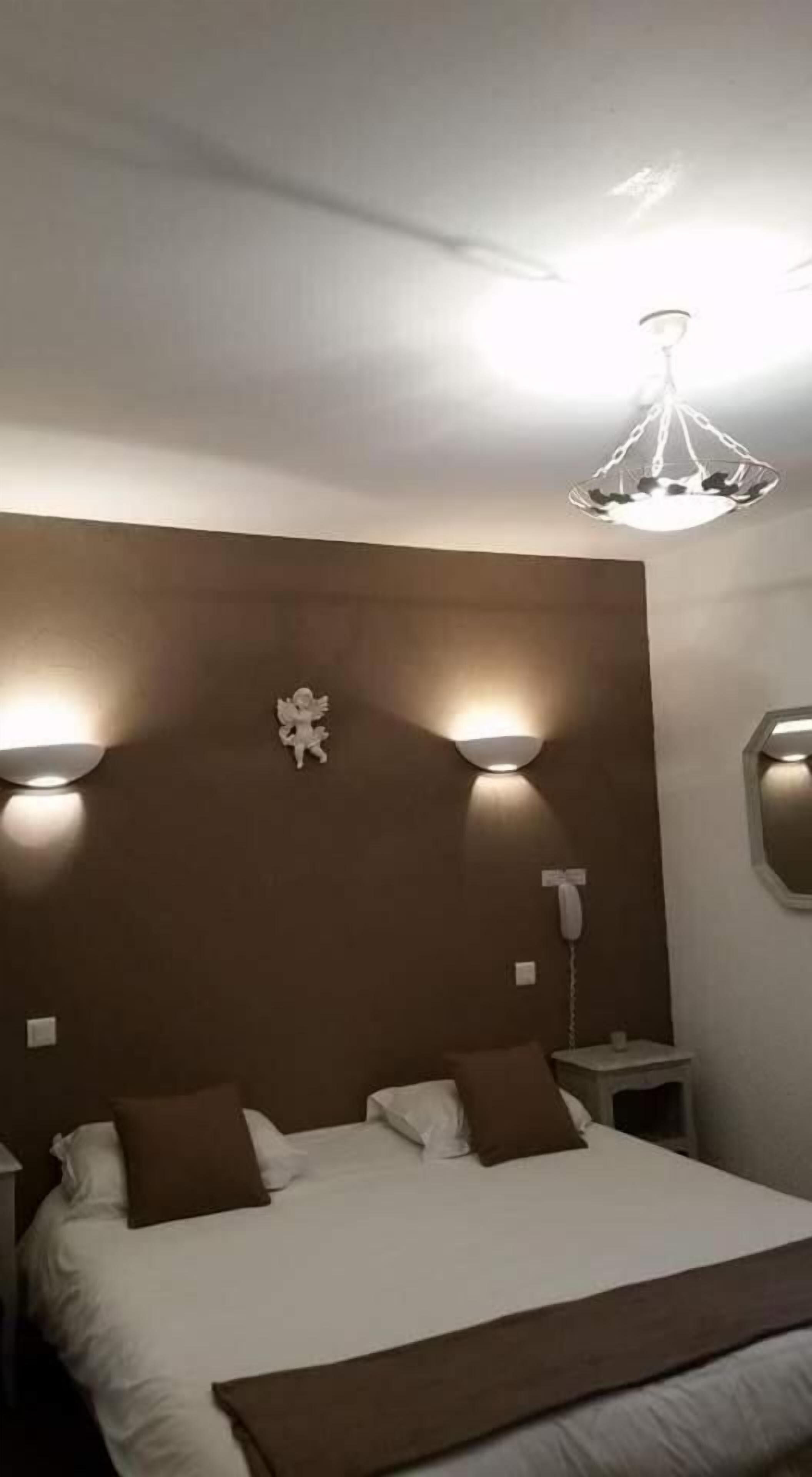 A hotel room with a large bed, two bedside tables, a wall-mounted telephone, and a ceiling light fixture.