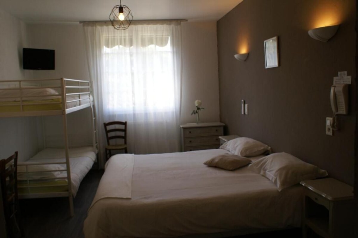 A hotel room with bunk beds, a desk, a chair, a bedside table, a lamp, and a TV.