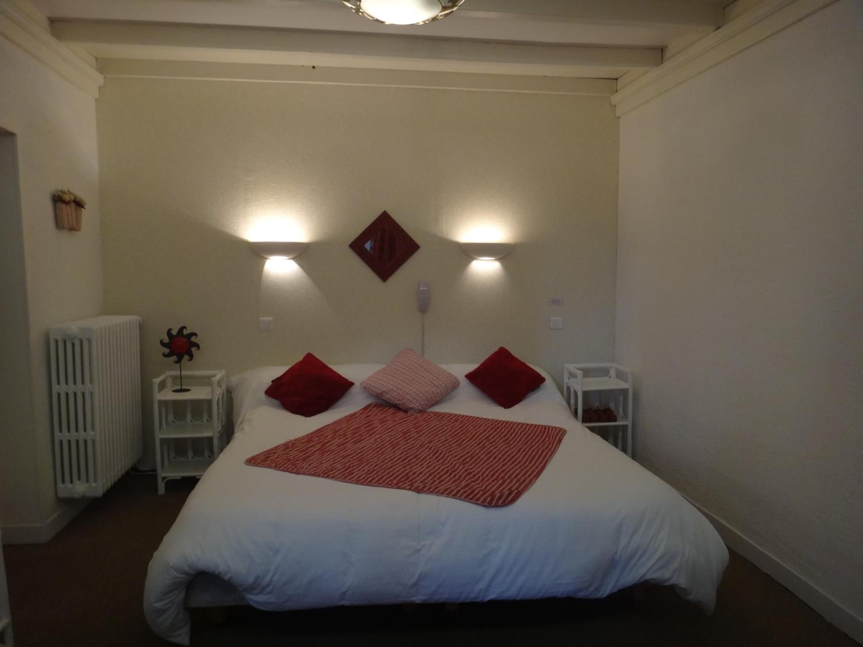 A bedroom with a large bed, two bedside tables, a radiator, and wall-mounted lights.