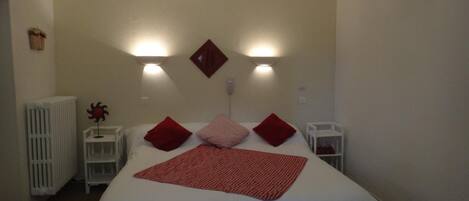 A bedroom with a large bed, two bedside tables, a radiator, and wall-mounted lights.