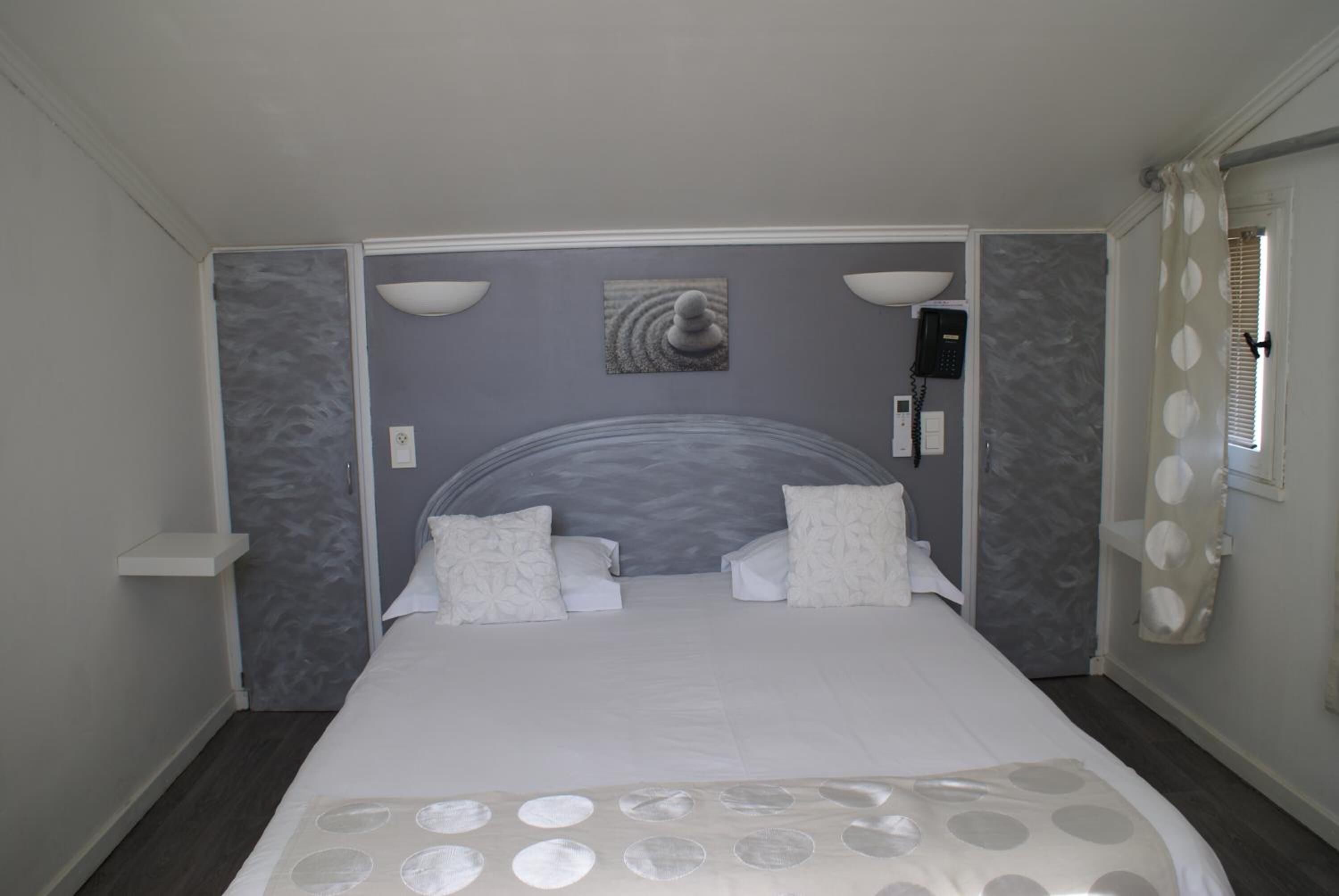 A bedroom with a bed, two wall-mounted lamps, a telephone, and a window with a curtain.