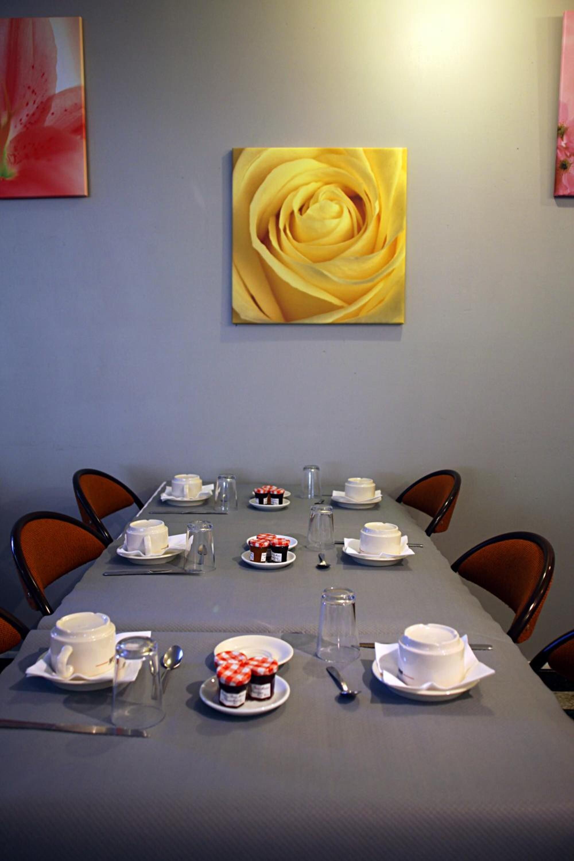 A dining table set for four with white tableware and a yellow rose painting above it.