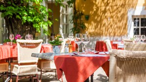 An outdoor dining area with wicker chairs and tables covered with red tablecloths. - Hôtel Le Petit Manoir Provence (Les Angles)
