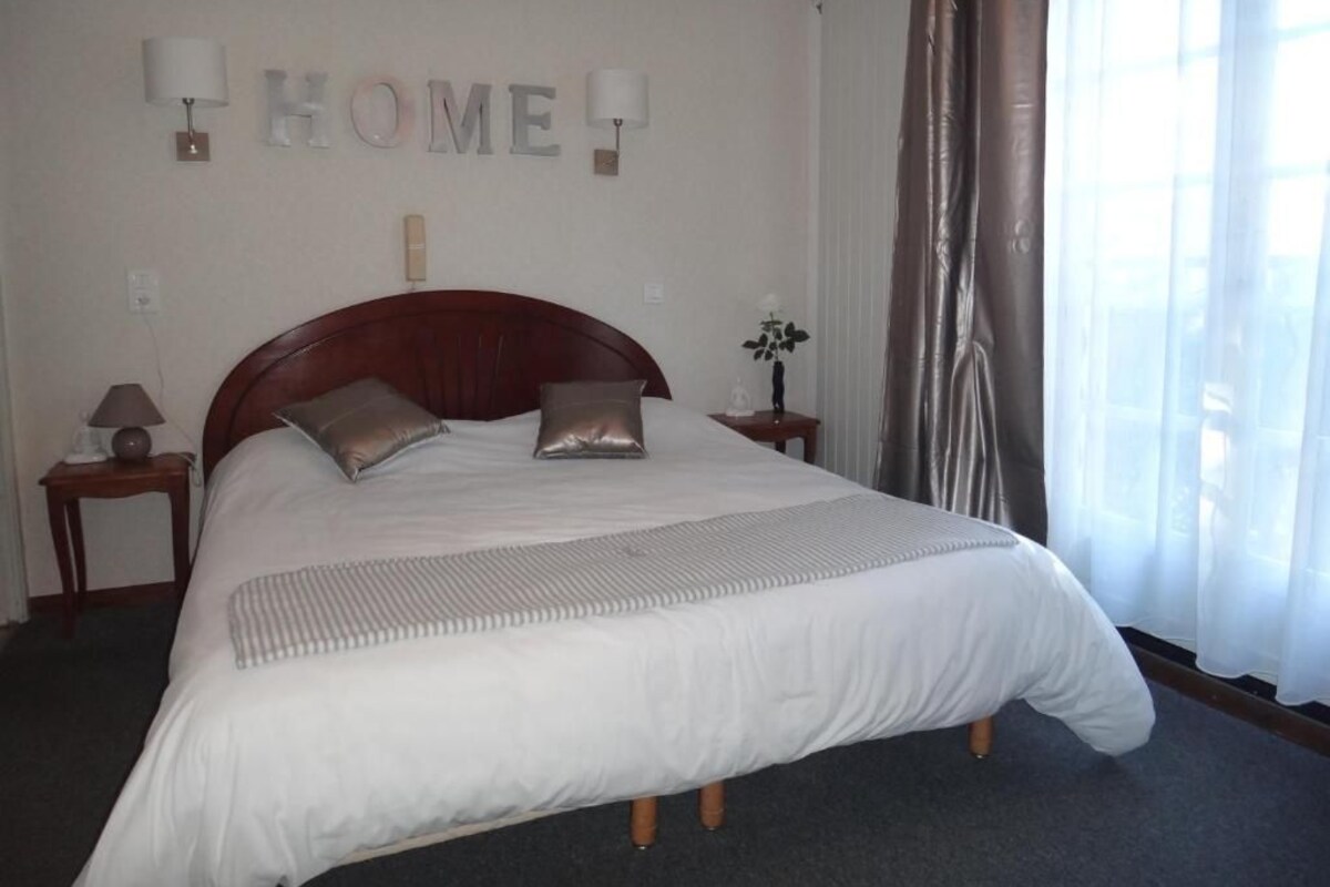 A neatly made bed with a wooden headboard, a bedside table with a lamp, and a wall-mounted sign that reads "HOME".