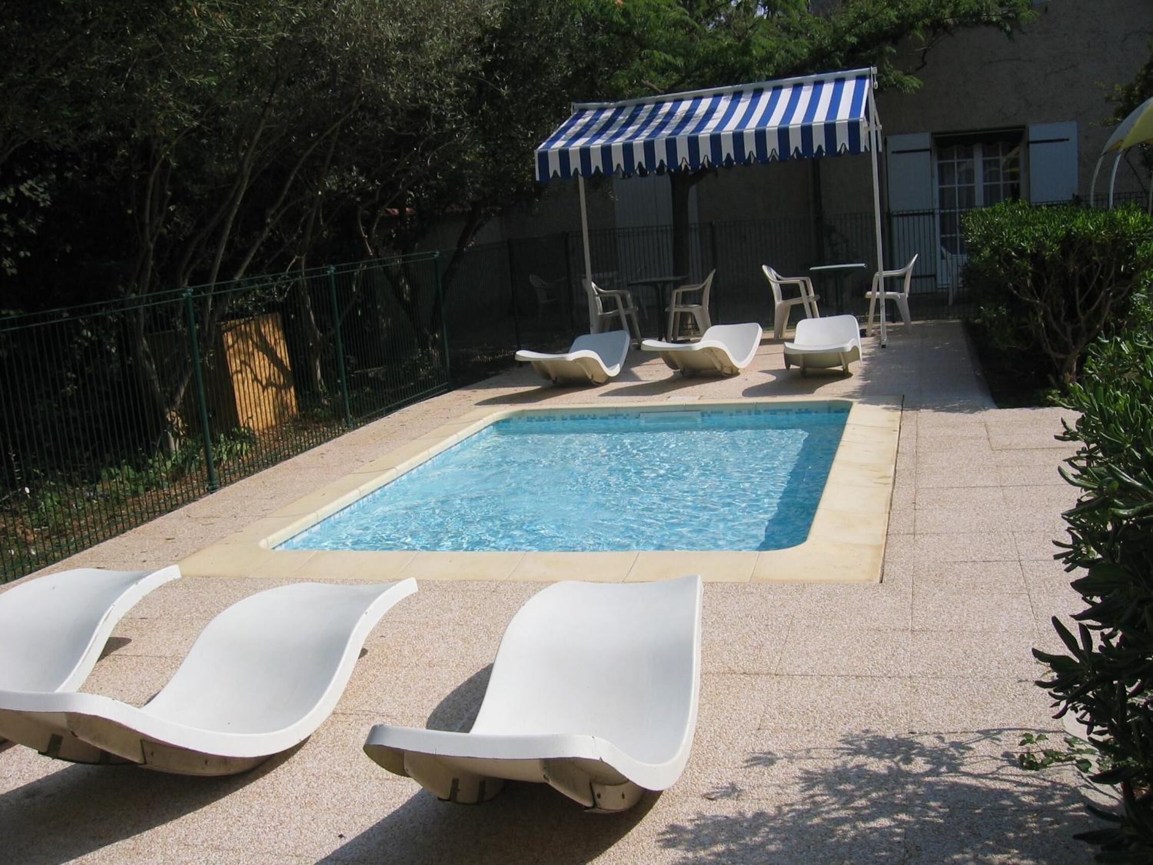 Una piscina con sillones de descanso y un toldo a rayas.