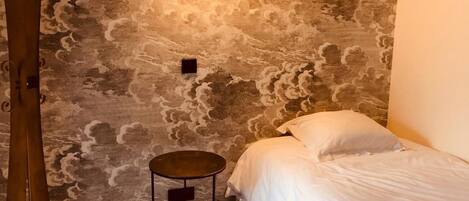 A bedroom with a bed, a round side table, a wall-mounted light, and a decorative wooden structure.