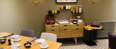 A dining area with a wooden table set for four, a buffet counter with various food items, and wall-mounted light fixtures.