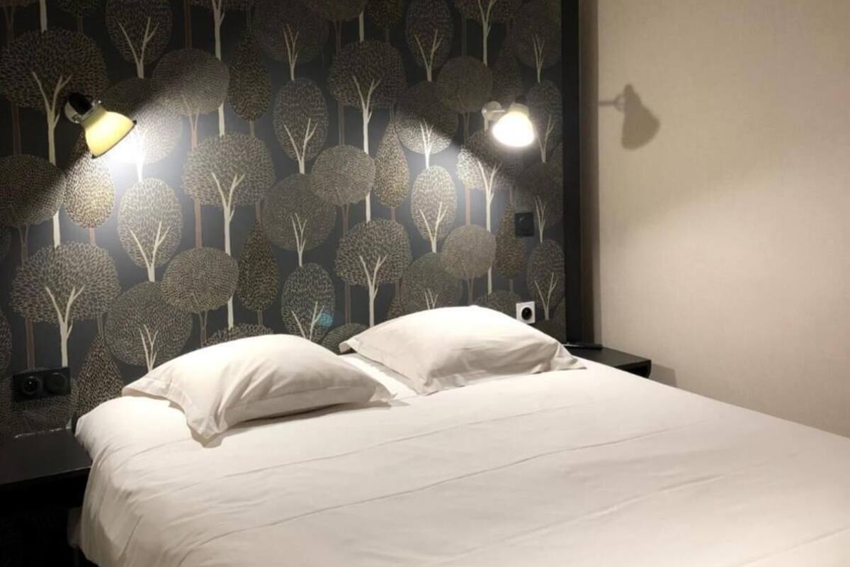 A hotel room with a large bed, two bedside lamps, and a wall with a tree pattern.