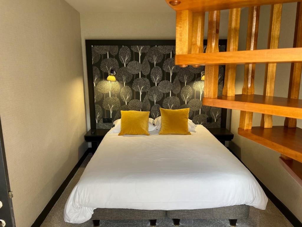 Camera d'albergo con un letto, due cuscini, una testiera decorata con un motivo a tema alberi e una panca in legno.