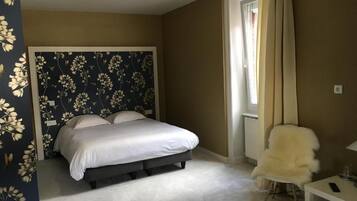 A bedroom with a bed, a chair, a table, and a window with curtains.