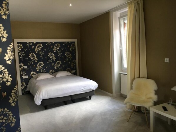 Un dormitorio con cama, una silla, una mesa y una ventana con cortinas.